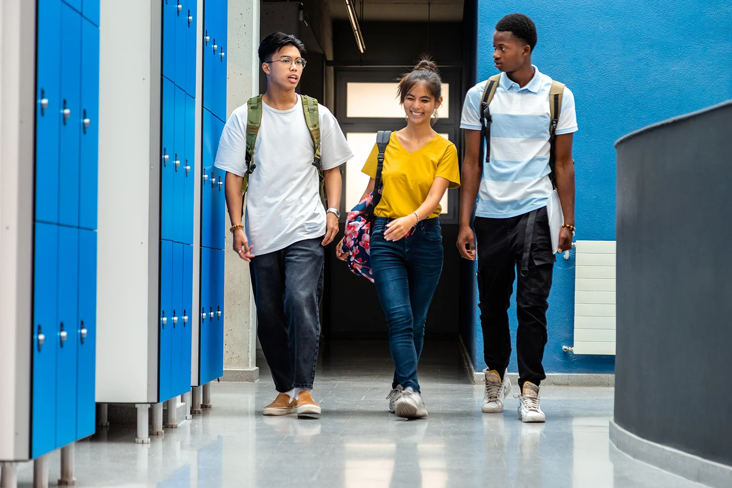 three students walking in hallway with lockers
